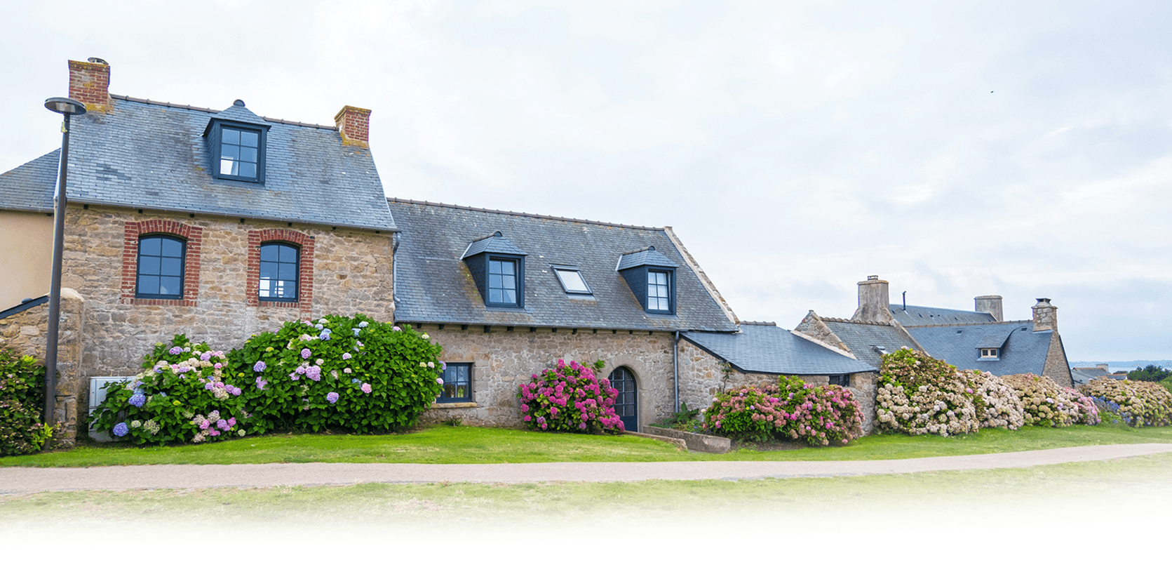 Longère bretonne en pierre aux fenêtres posées par Finestra, bordée d'hortensias